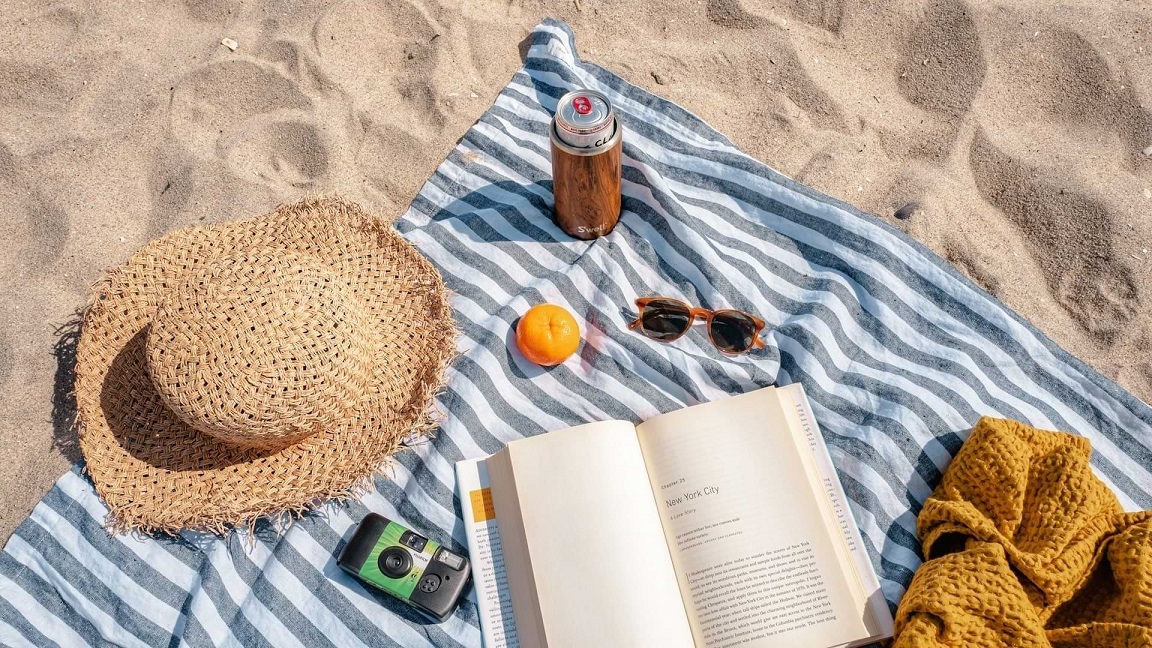 Zomerse stranddag met zonnehoed, boek en drankje in het goedkoopste land van Europa voor zonvakantie